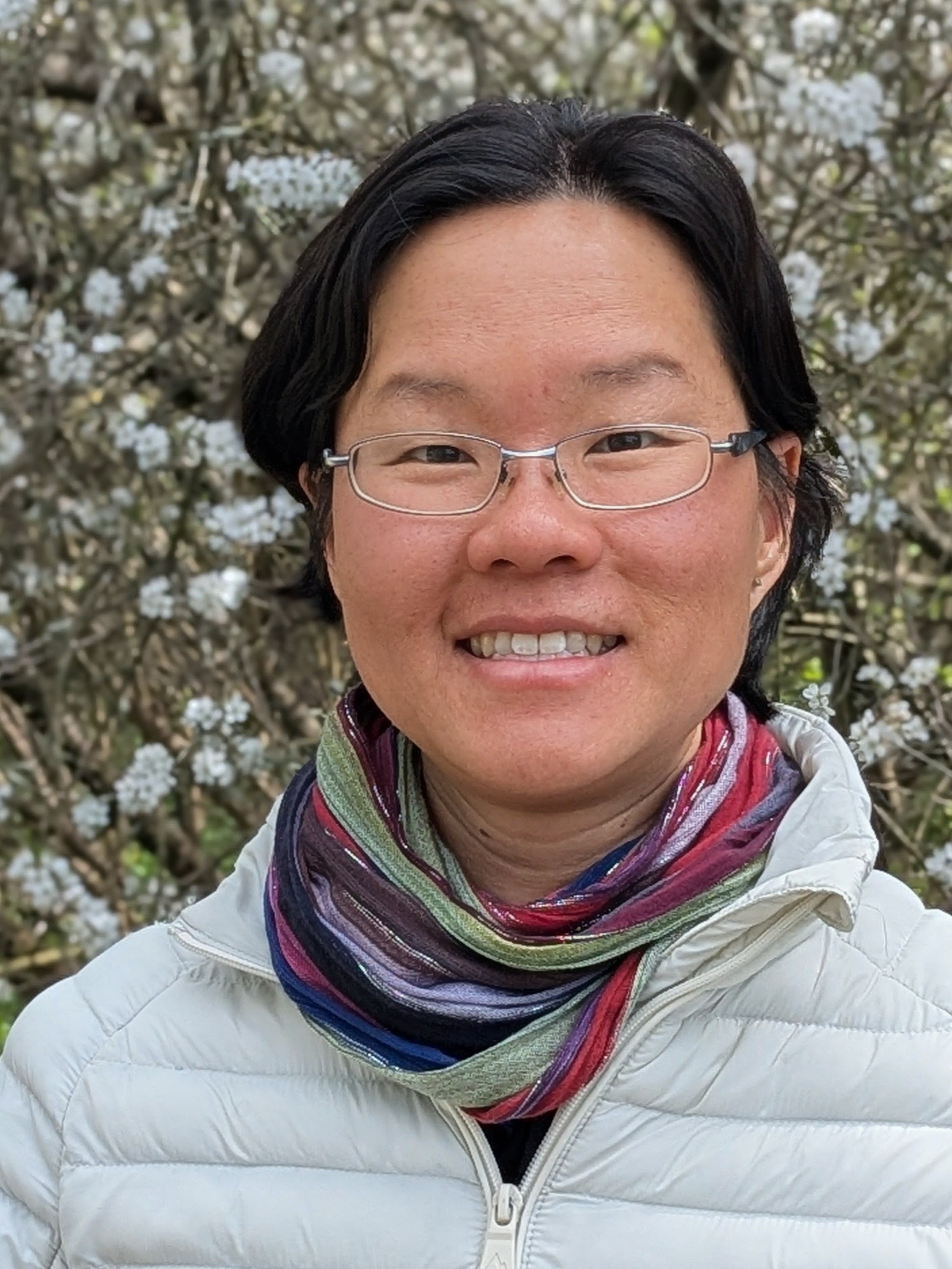 Portrait of Hannah, an ethnic Chinese woman with short hair and glasses, wearing a white puffer jacket and a colourful scarf