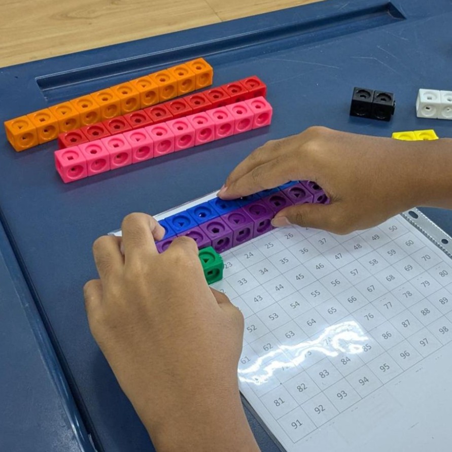 Closeup of a student's hands placing Mathlink cubes on a hundreds chart.